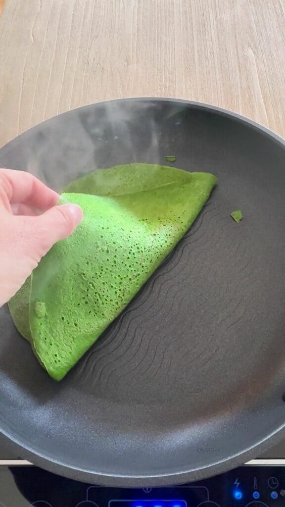 Using spatula to flip spinach wrap in pan, showing golden cooked side